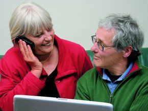 Casal idoso em frente a um celular olhando um para o outro enquanto a mulher fala ao telefone